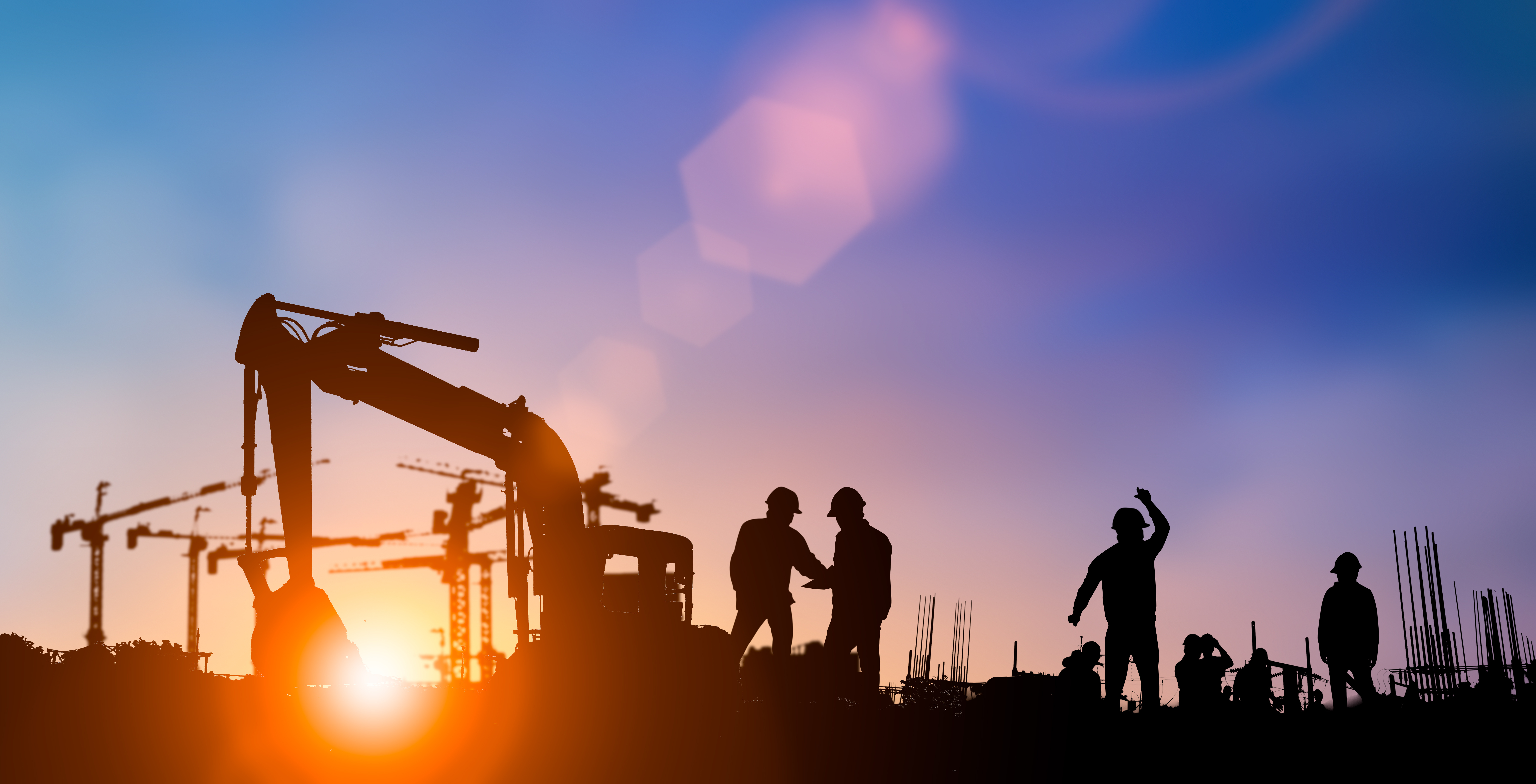 Silhouetted construction workers and cranes at sunset on a building site