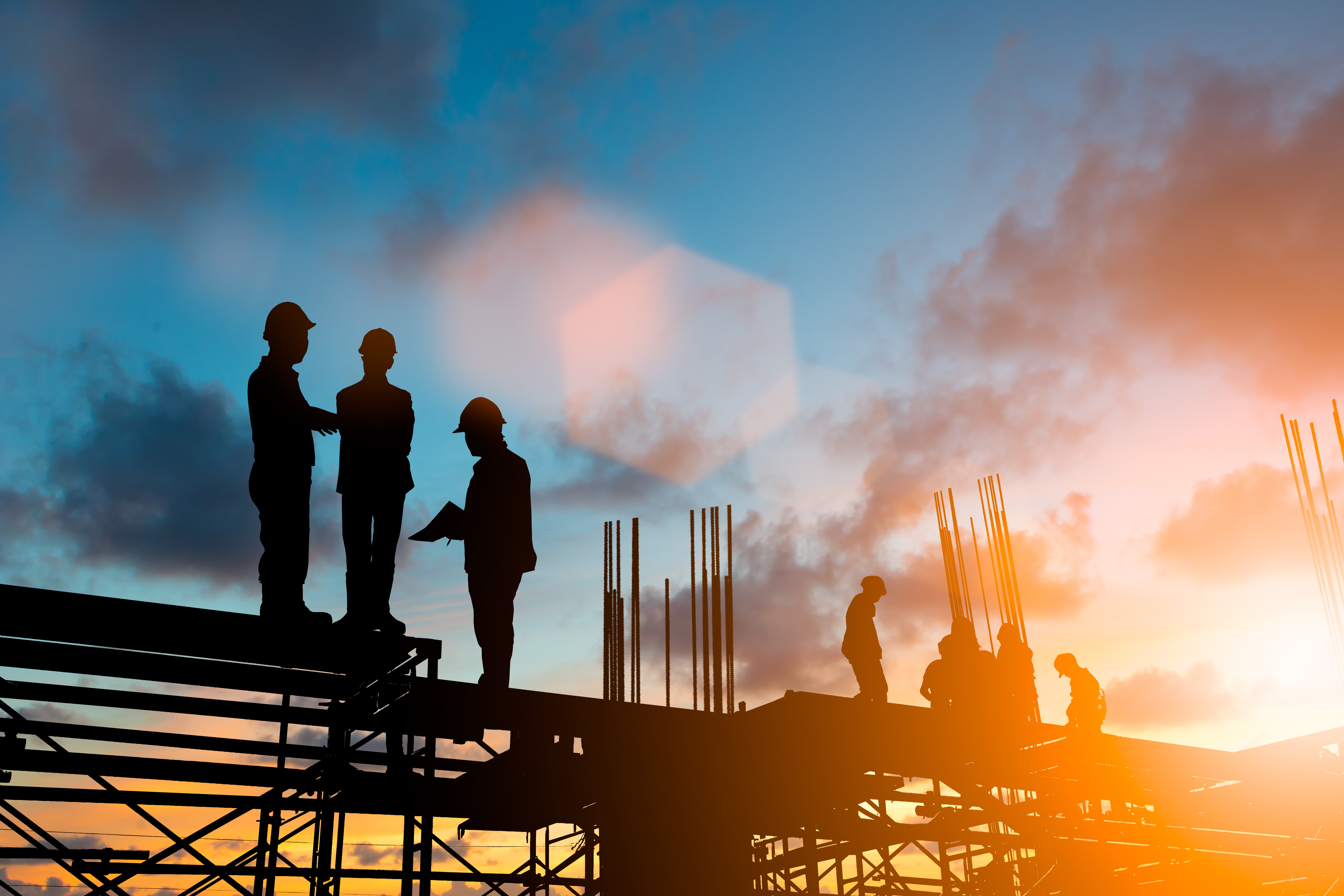 Construction workers on scaffolding at sunset reviewing plans on active job site
