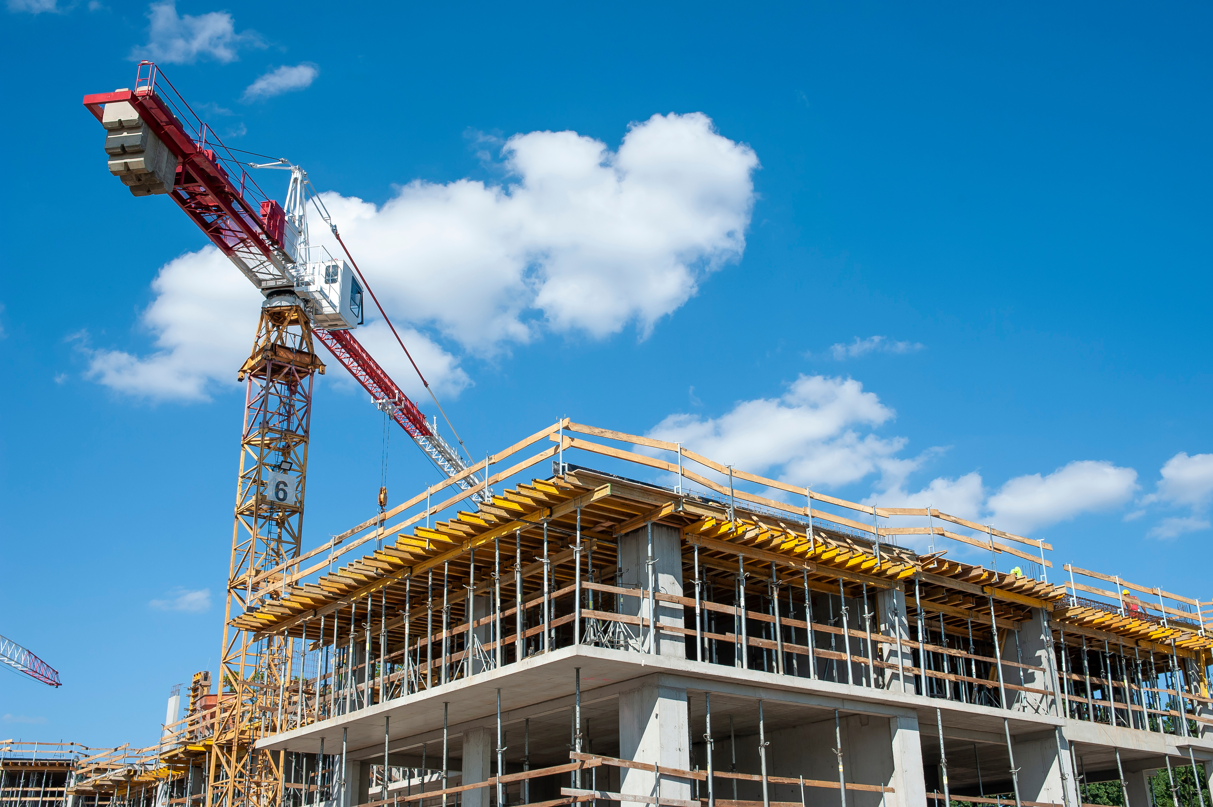 Construction site with concrete building frame, yellow scaffolding, and red tower crane against blue sky