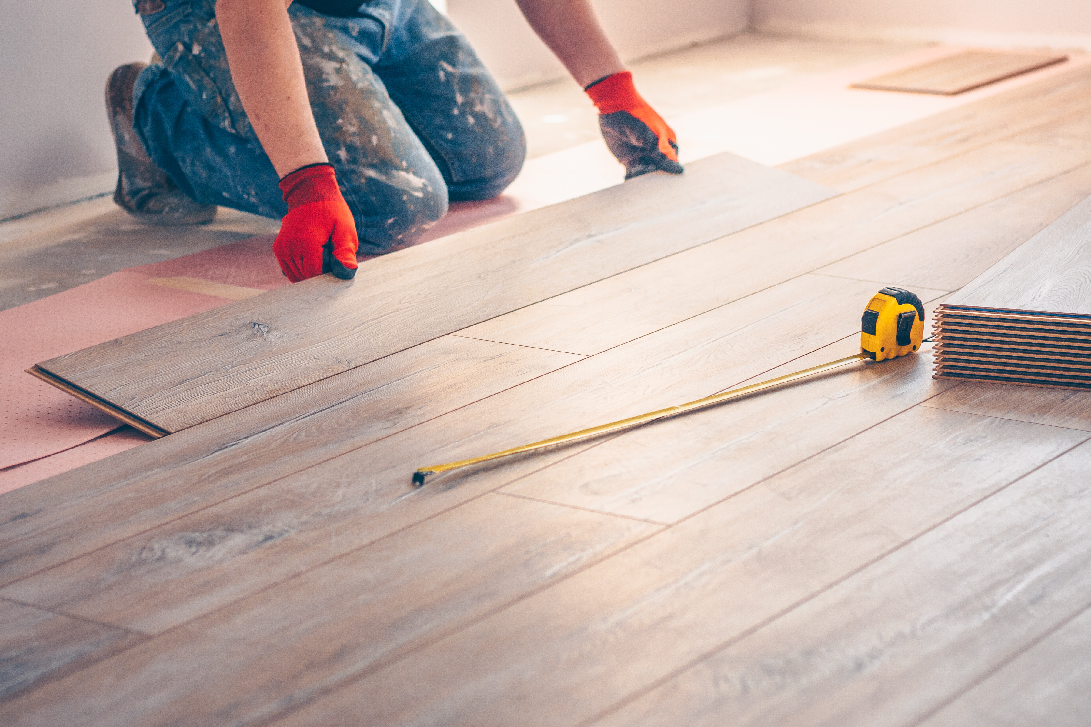 Worker in red gloves installing laminate flooring planks with tape measure and tools